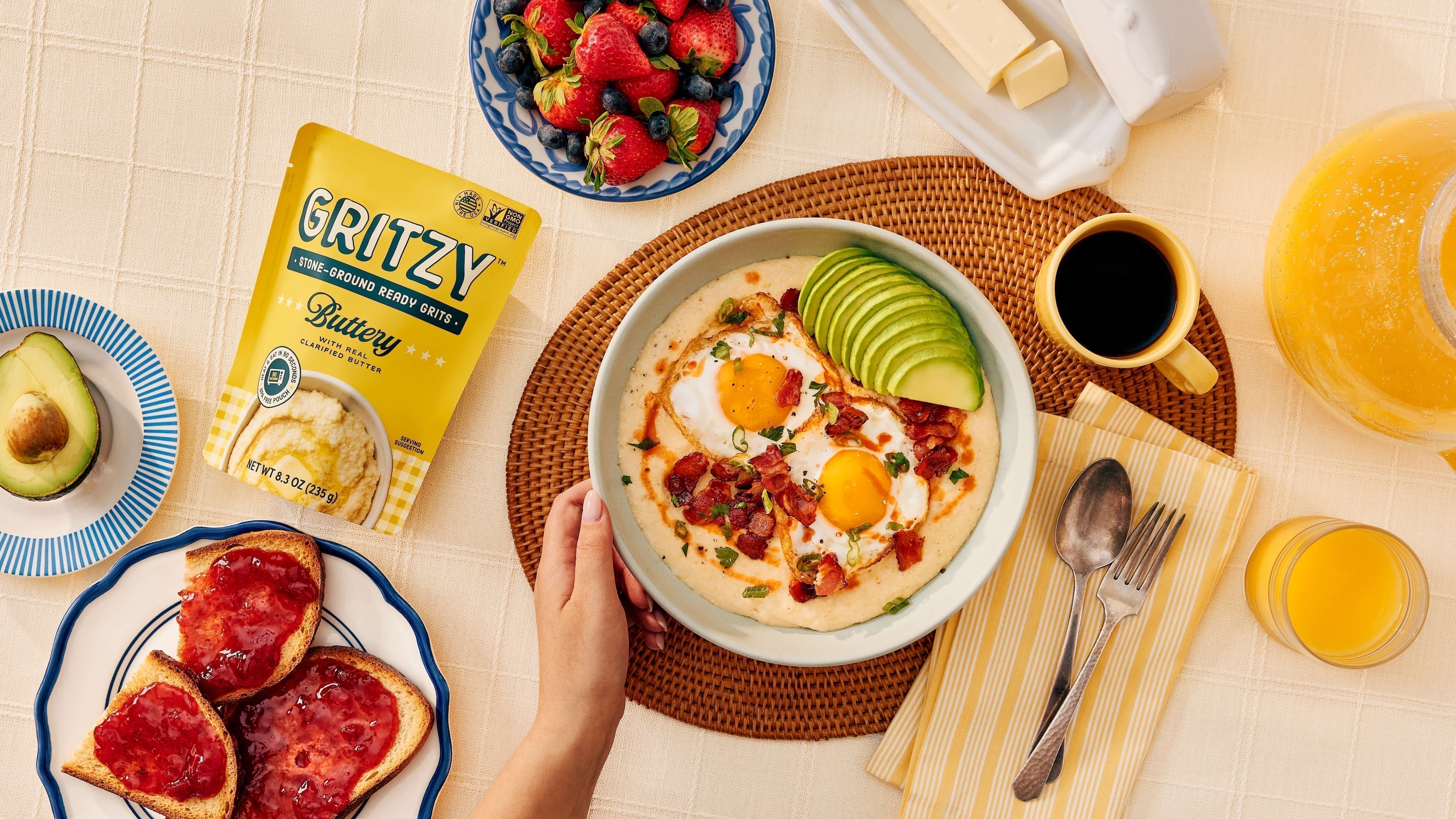 Bowl of Gritzy Buttery grits served with toast, eggs, and fresh fruit on a yellow background